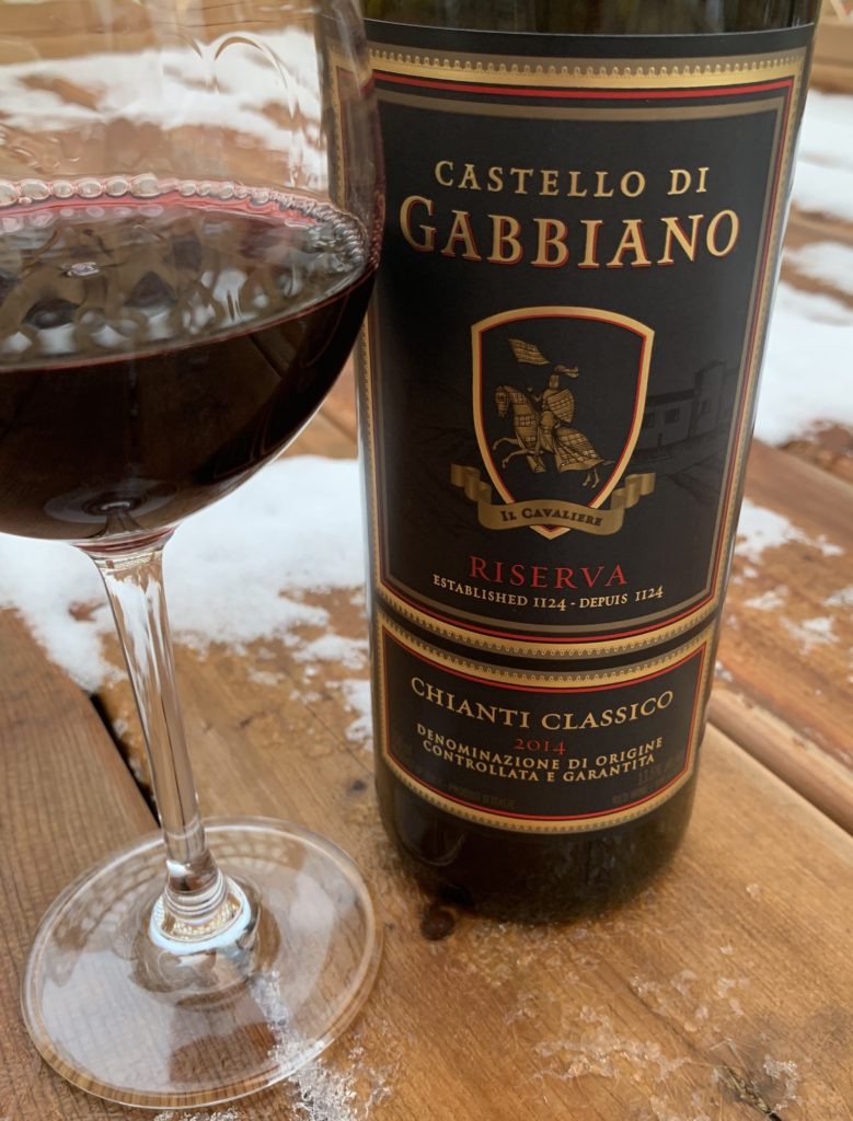 a glass of red wine sitting beside a bottle of Gabbiano Chianti Classico Riserva with snow in the background