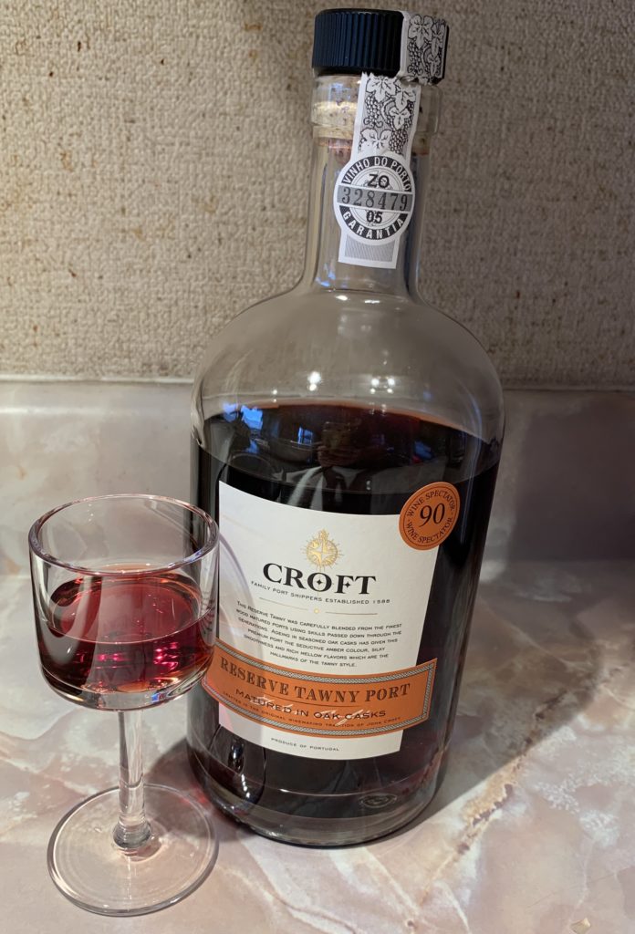 a small glass of port wine sitting beside a bottle of Croft Reserve Tawny Port
