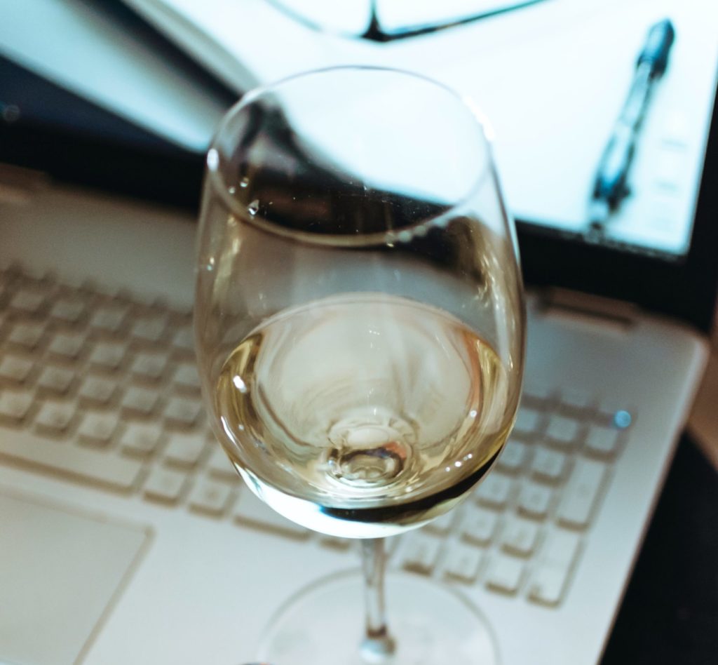 a glass of white wine sitting on the edge of an open laptop