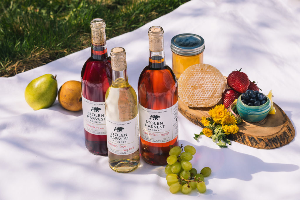 three bottles of wine on a white tablecloth with fruit and honeycomb behind