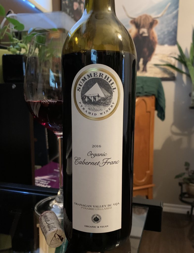 a bottle and glass of red wine sitting on a glass desk with a picture of a cow and some green plants in the background