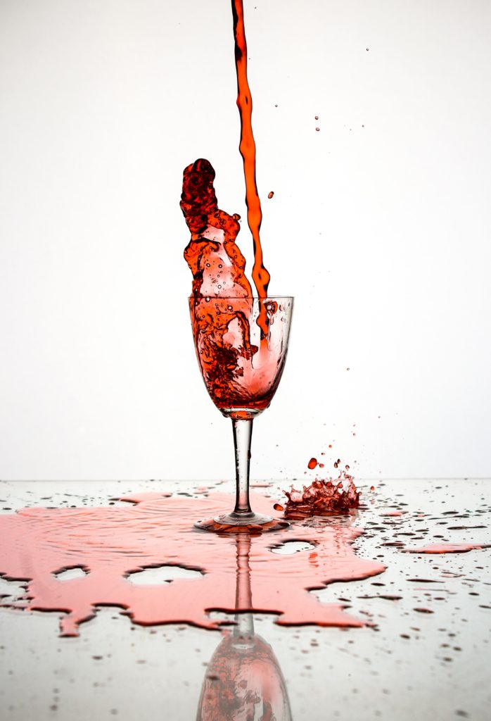 a stream of red wine being poured into a glass with wine splashing out and pooling on the table